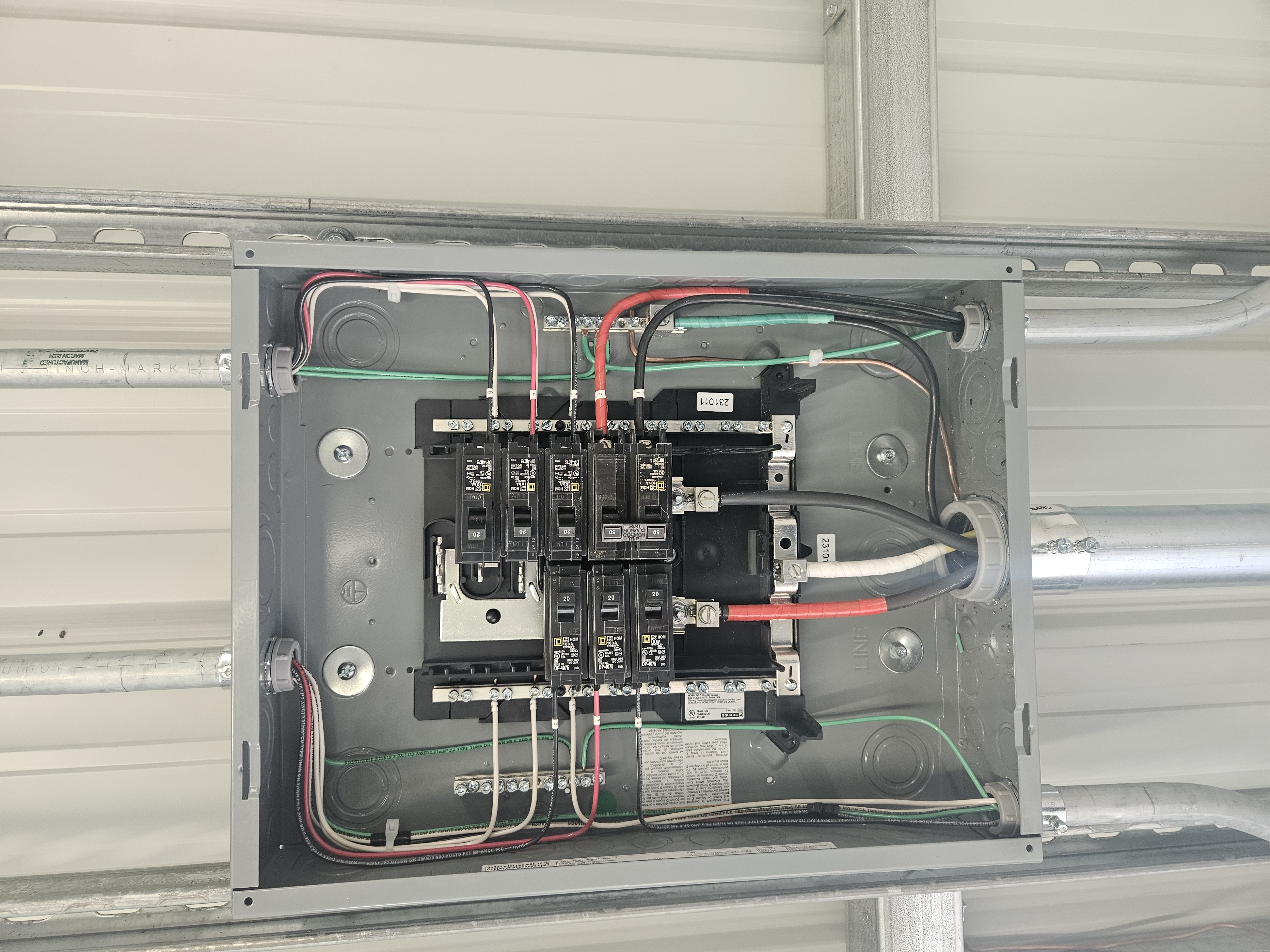 Open electrical sub-panel with conduit on corrugated metal wall
